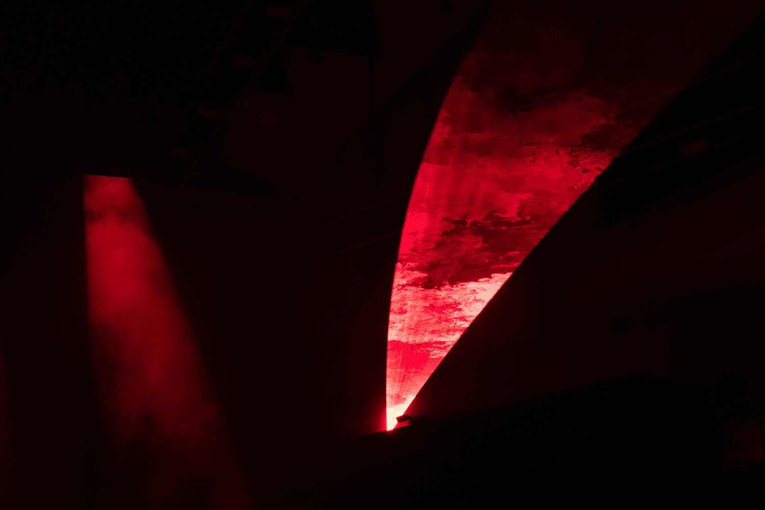 Sliver of red light cutting diagonally across a dark stage curtain.