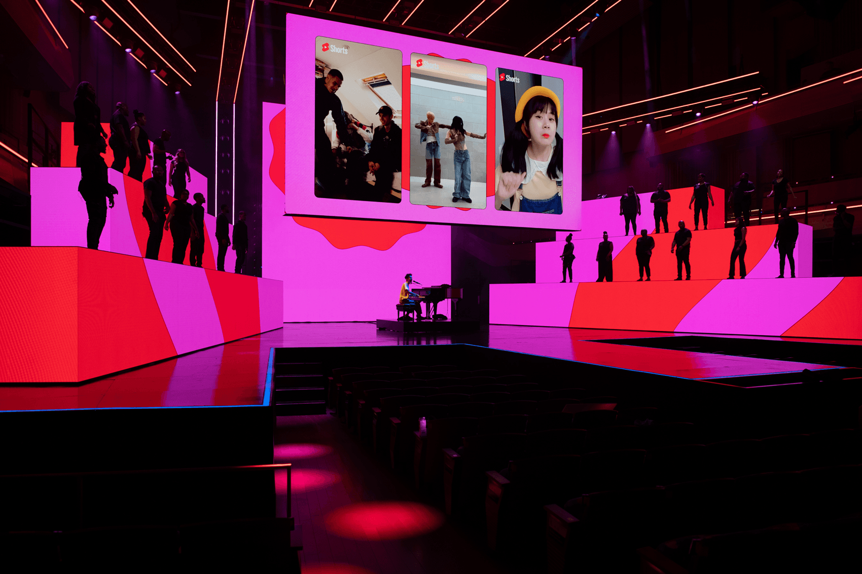 Pink-lit stage with angled panel walls and rows of silhouetted audience members below.