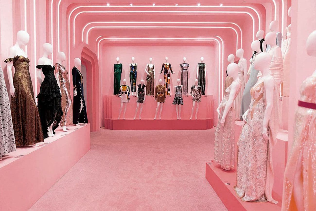 Pink curved corridor lined with mannequins dressed in evening gowns.