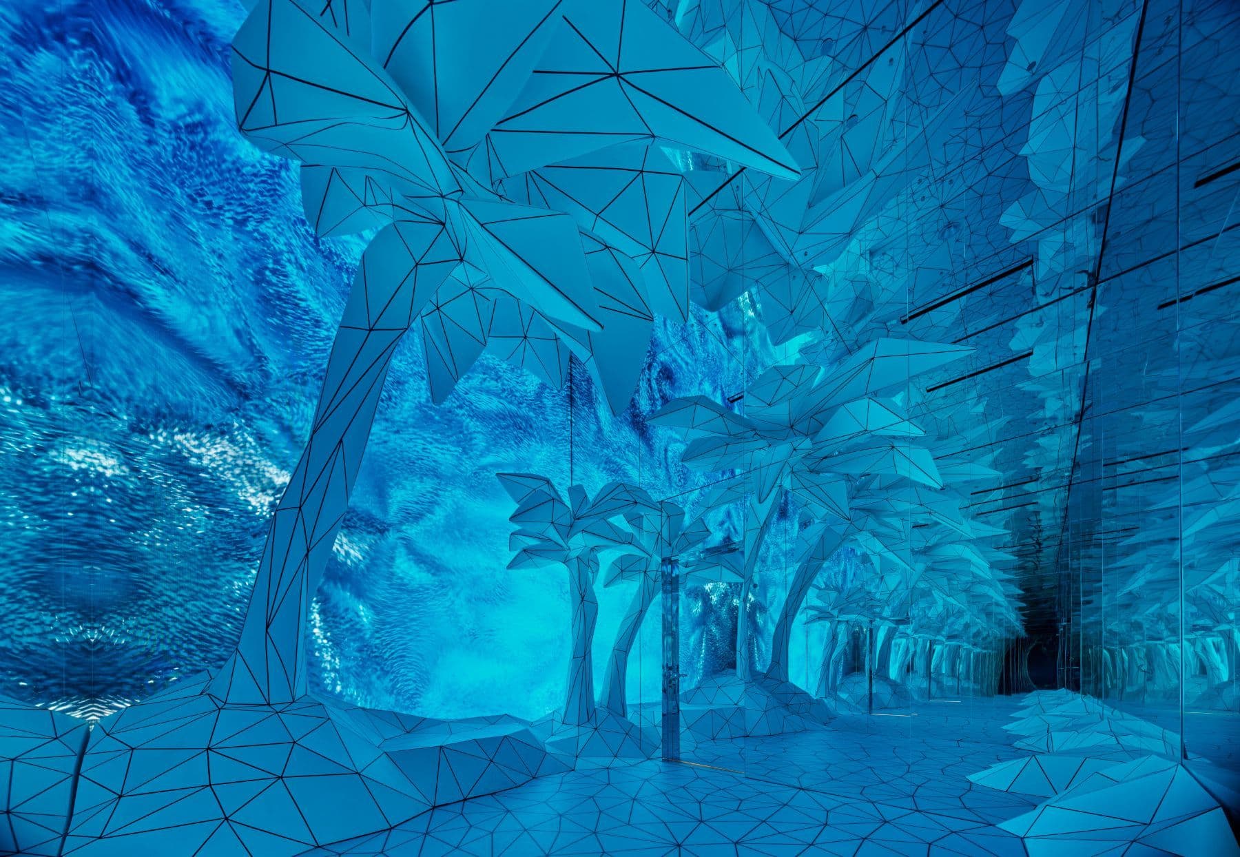 Immersive blue-lit tunnel installation with faceted low-poly palm trees and reflective floor.