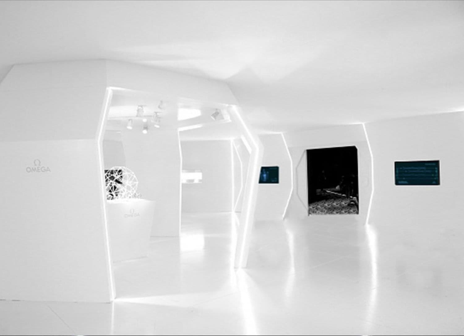 Angular white exhibition space with an OMEGA sign, a display pedestal, and a dark doorway.