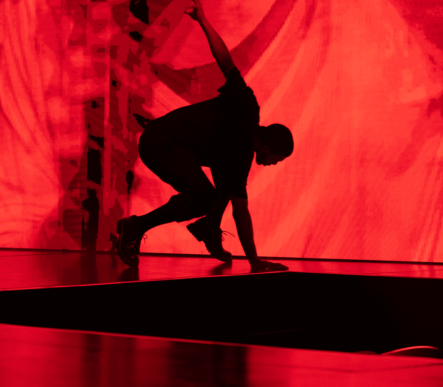 Silhouetted dancer crouched low against a red-lit curtain backdrop.