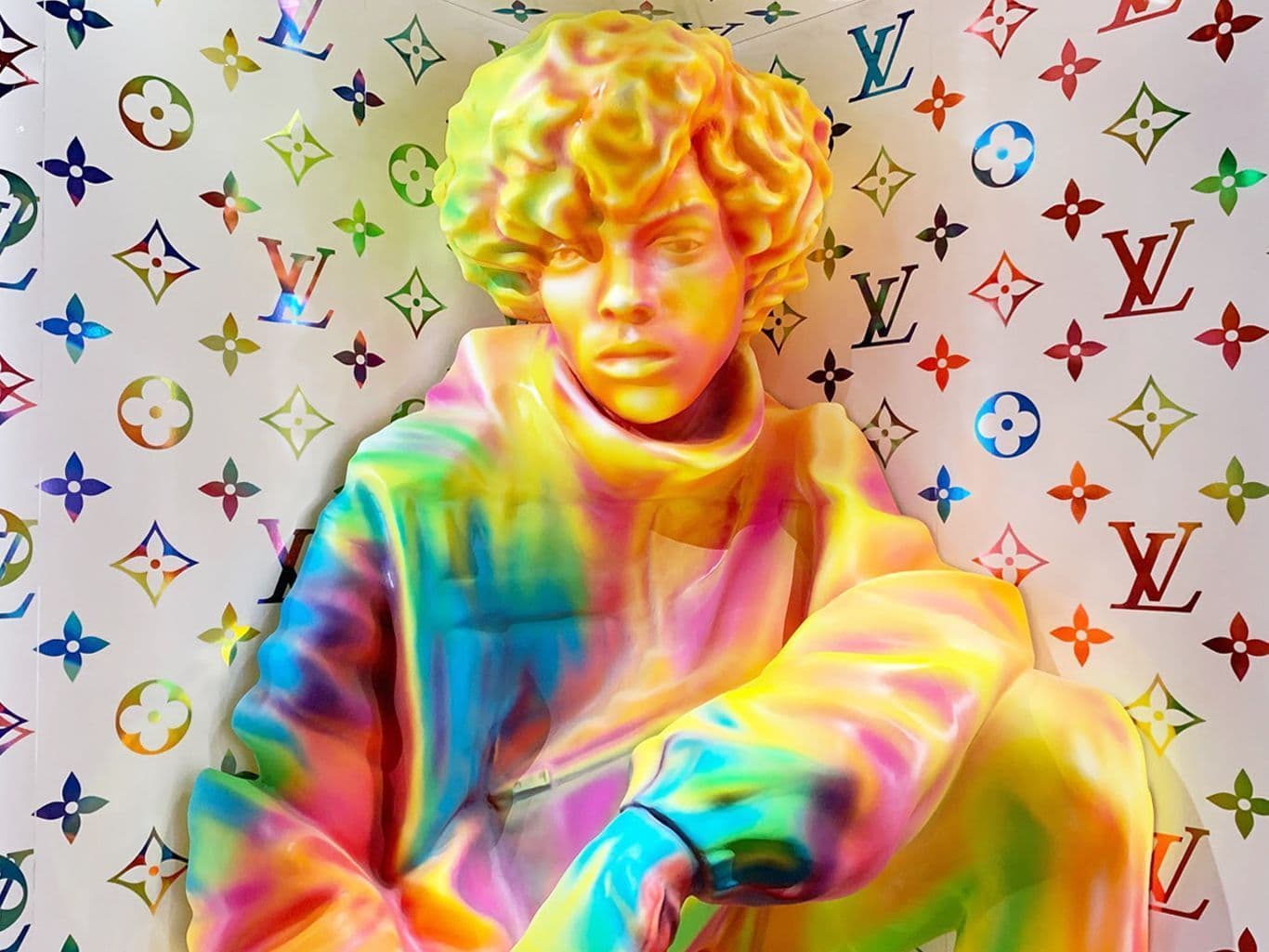Close-up of a rainbow-colored bust sculpture against a Louis Vuitton monogram wallpaper.