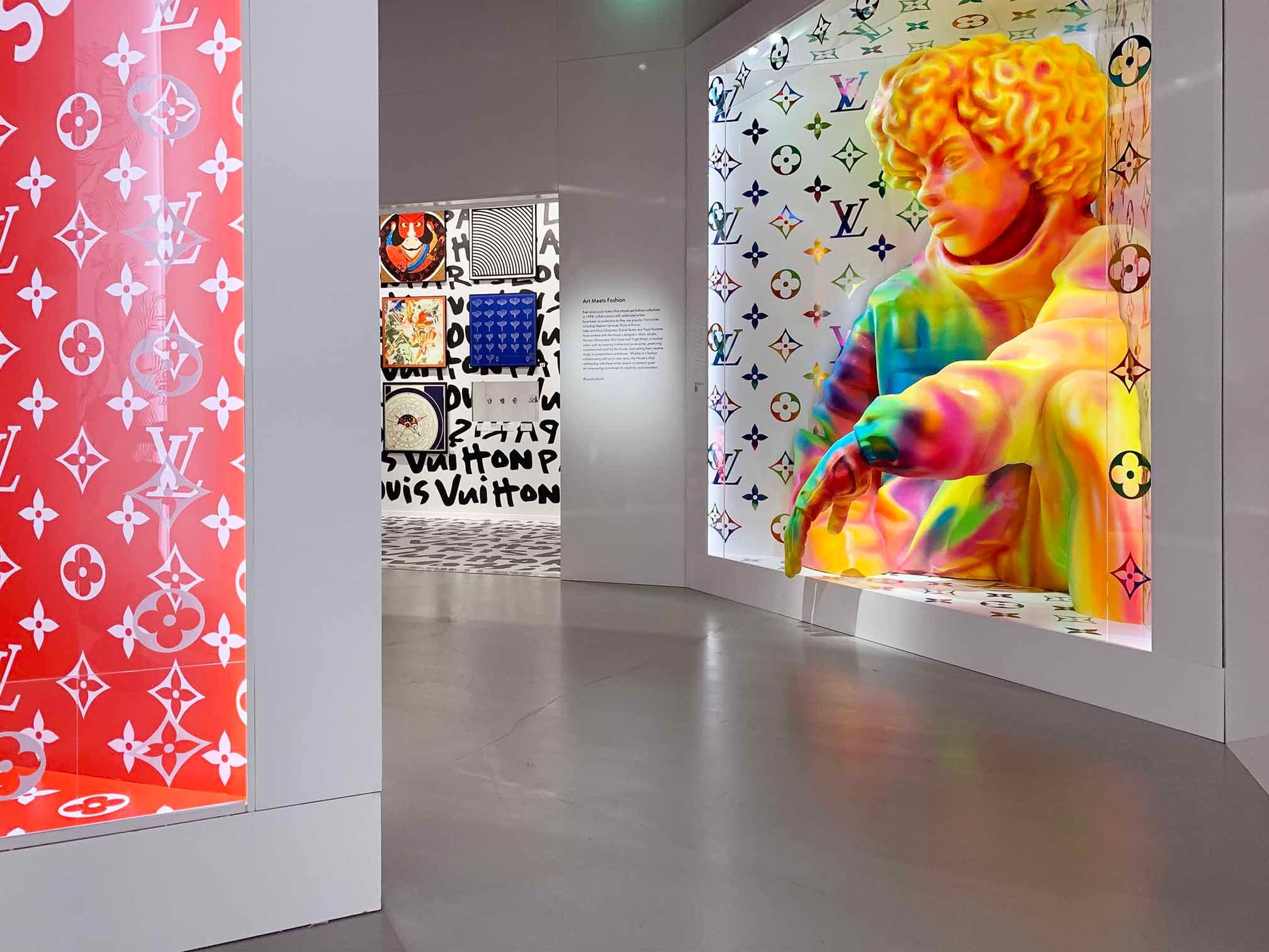 Gallery corridor lined with Louis Vuitton monogram-patterned wall panels and a large framed portrait.