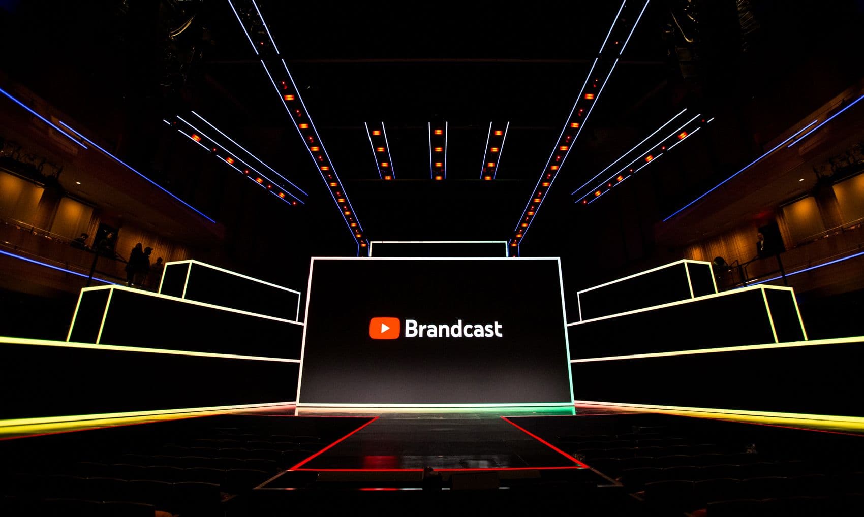 Brandcast logo displayed on a stage screen framed by yellow-lit angular panels and empty arena seating.