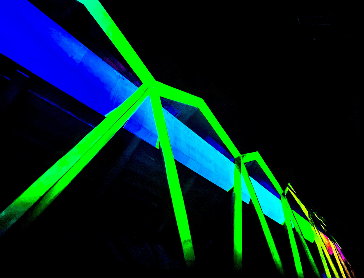 Close-up of crossing blue, green, and pink neon light beams on the installation's angular framework