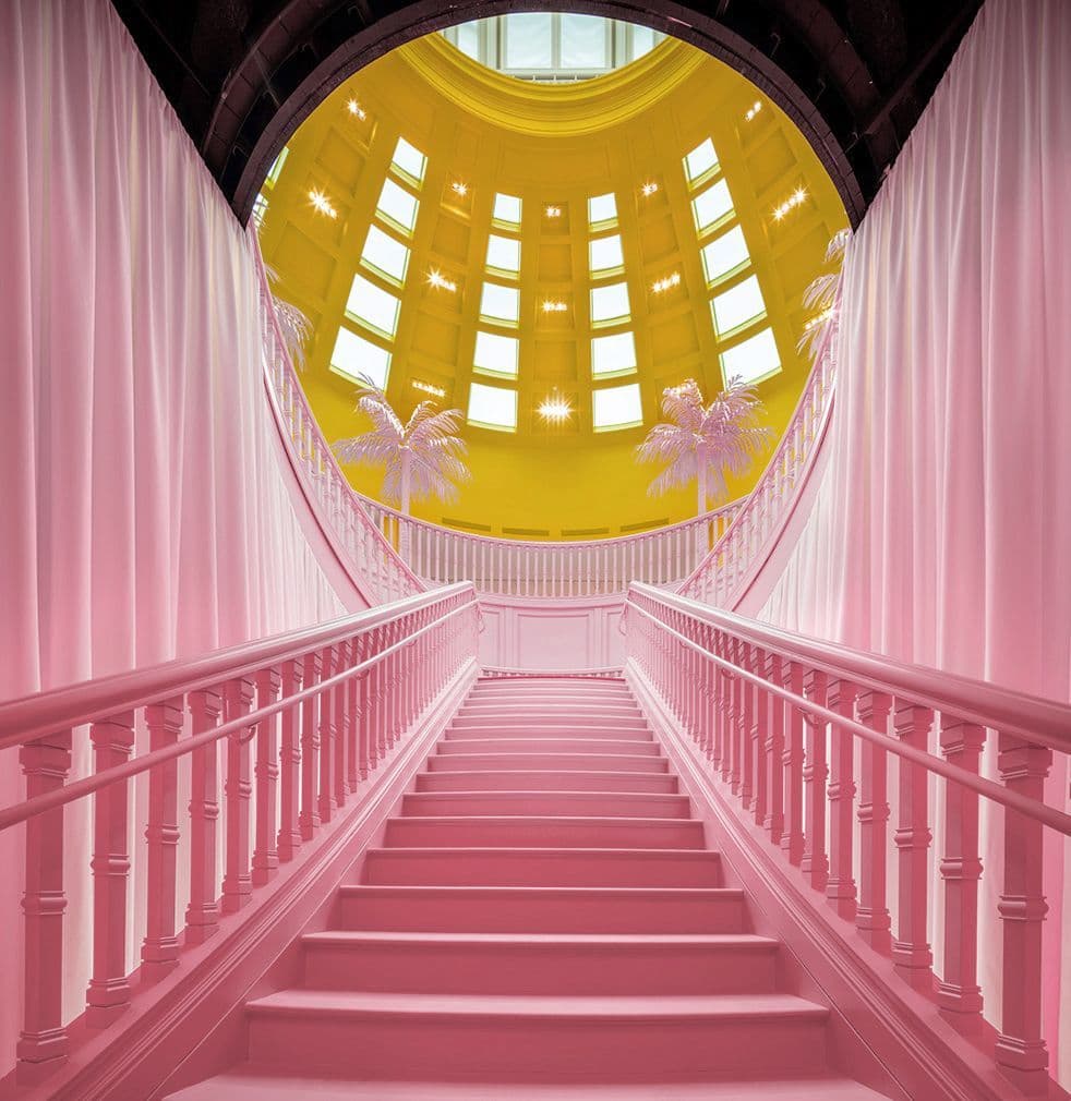 Pink staircase ascending toward a circular skylight glowing yellow at the top of a domed hall.