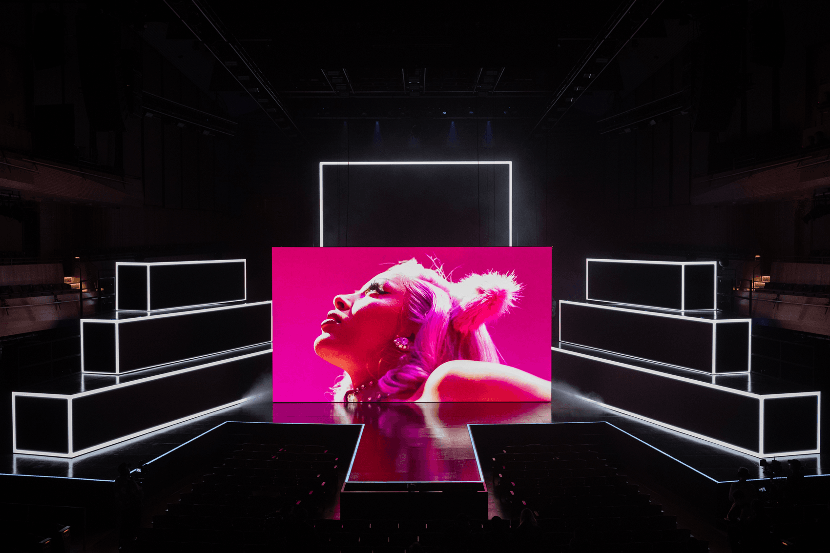 Bright pink LED screen showing a close-up of a performer, flanked by angular white panel walls.