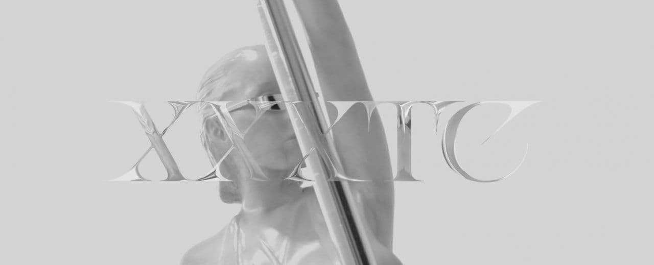 Black-and-white grainy image of a figure holding a bow-like object, overlaid with the stylized wordmark "XXXTC".